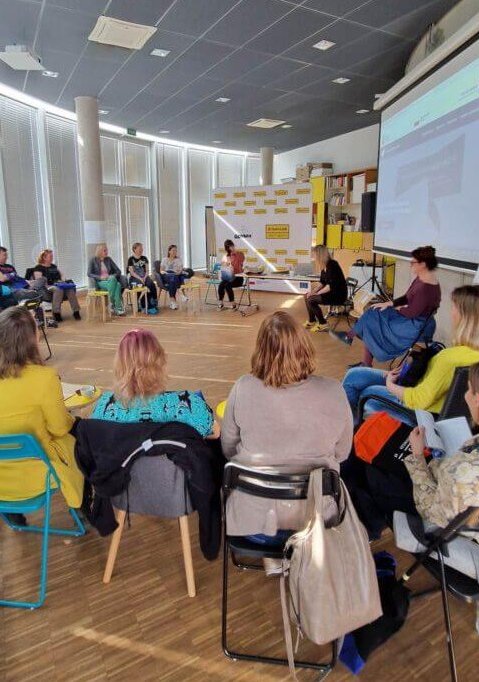 Grupa kilkunastu osób siedzących w sali na krzesłach w kręgu